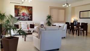 Ein modernes Wohnzimmer mit Sofa, Couchtisch und Essbereich. Übertöpfe und ein Gemälde zieren die Wand.