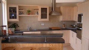 Una cocina con armarios de madera, una encimera negra y tres taburetes de madera.
