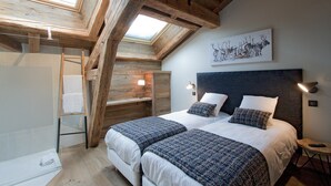 Ein Schlafzimmer mit zwei Betten, einem Oberlicht, Holzbalken, einem Gemälde und Nachttischlampen.