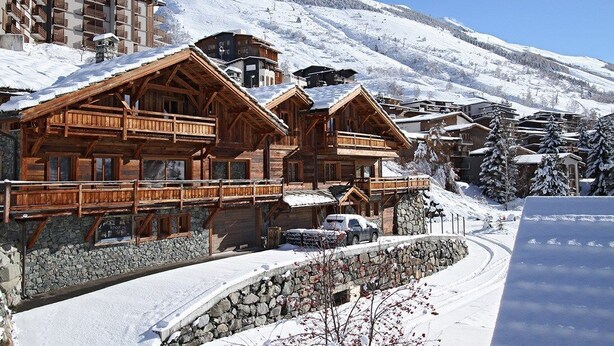 Ein Chalet-ähnliches Gebäude aus Holz mit Balkonen, umgeben von schneebedeckten Bergen und blauem Himmel.