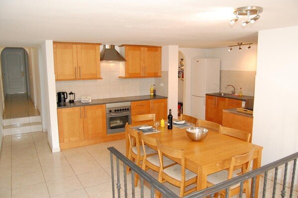Una cocina moderna con armarios de madera, horno integrado y un comedor con mesa y sillas de madera.