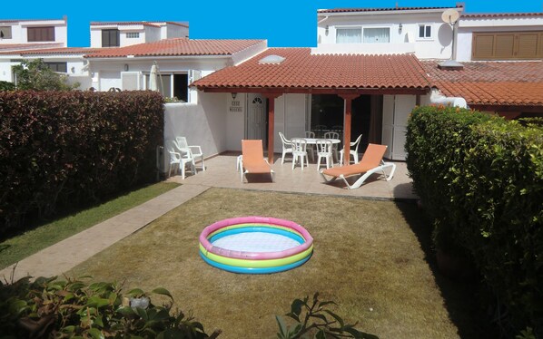 A residential property with a small backyard, a swimming pool, outdoor furniture, and a well-maintained lawn.