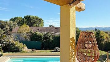 Un espace aménagé au bord de la piscine, avec une pergola en bois, un grand saladier en verre et un évier en métal.