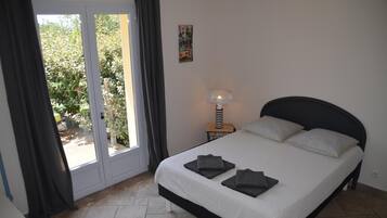 Une chambre à coucher comprenant un lit, une table de chevet, une lampe et une vue sur un jardin, accessible par une porte coulissante.