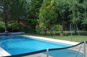 Une piscine rectangulaire entourée d’une clôture de sécurité, bordée d’arbres et d’une pelouse.