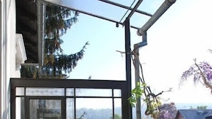 Ein Wintergarten mit weißem Tisch und Stühlen, einem Blumenstrauß und Blick auf ein rotes Haus und Bäume.