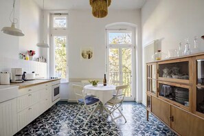 Una cocina con armarios blancos, una mesa de comedor con sillas, una cafetera y una ventana con vistas a árboles.