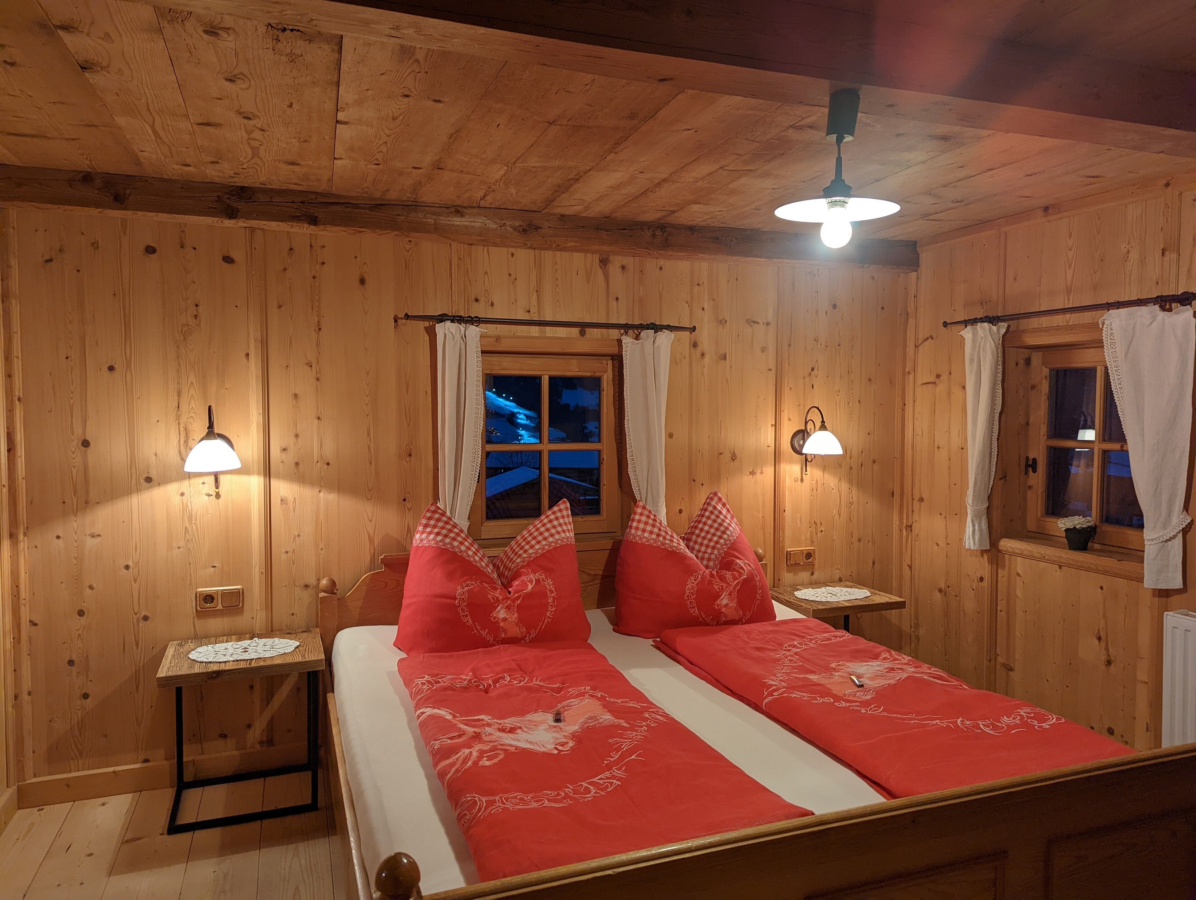Une pièce en bois avec deux lits, une table de chevet, une table avec un chemin de table et une fenêtre avec des rideaux.