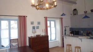 Een keuken met een houten tafel, barstoelen, een kroonluchter en een raam met gordijnen.