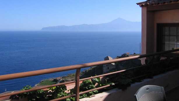 Un balcon avec vue sur la mer et une montagne qui se profile à l’horizon.