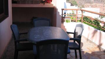 An outdoor patio with a stone table and chairs, a stone oven, and a view of a mountainous landscape.