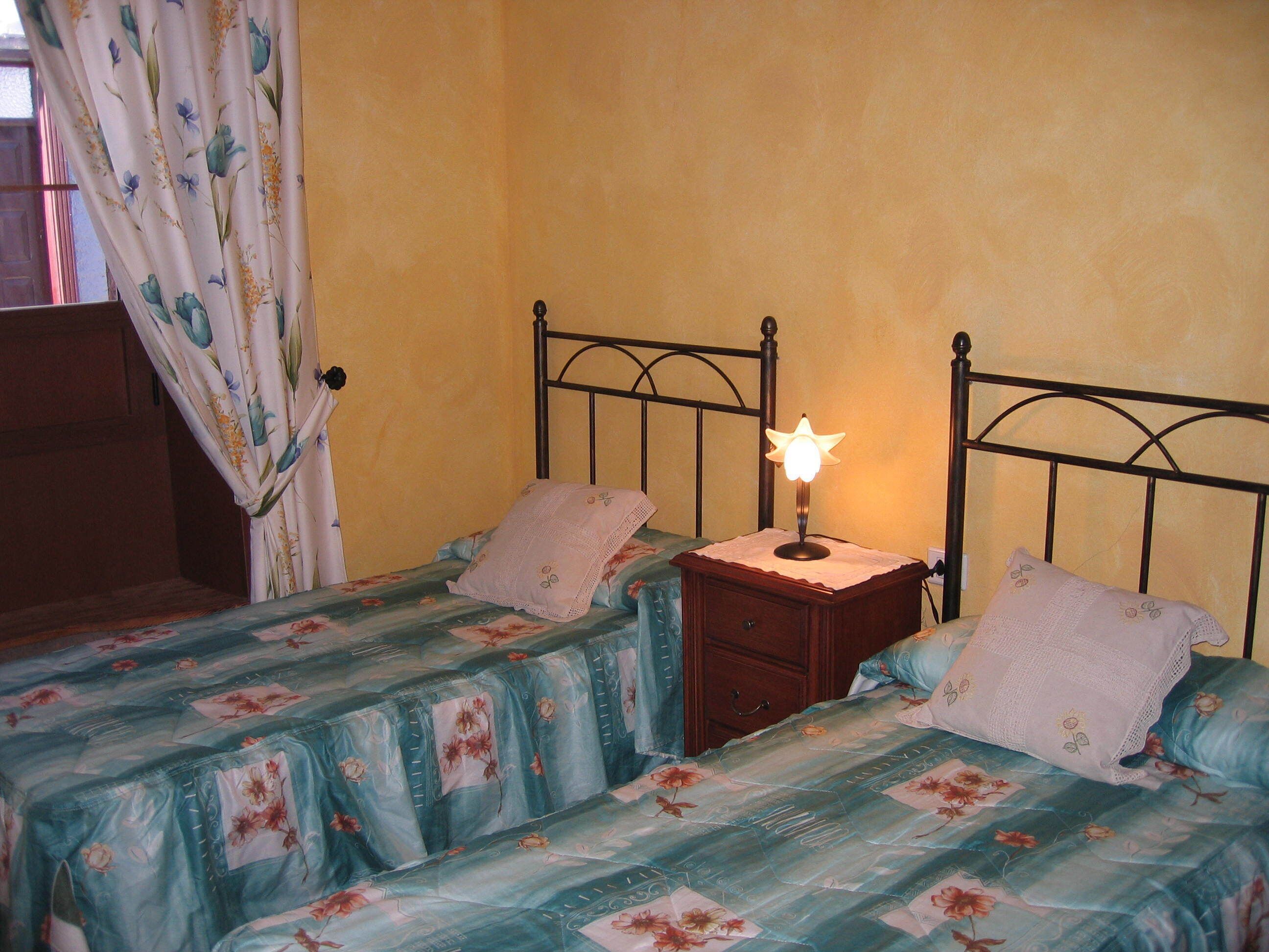 Una camera da letto con due letti singoli, un comodino con lampada e una finestra con tende.