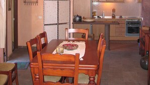 Un coin repas avec une table et des chaises en bois, un lustre, et une cuisine dotée de meubles et d’appareils électroménagers en bois.