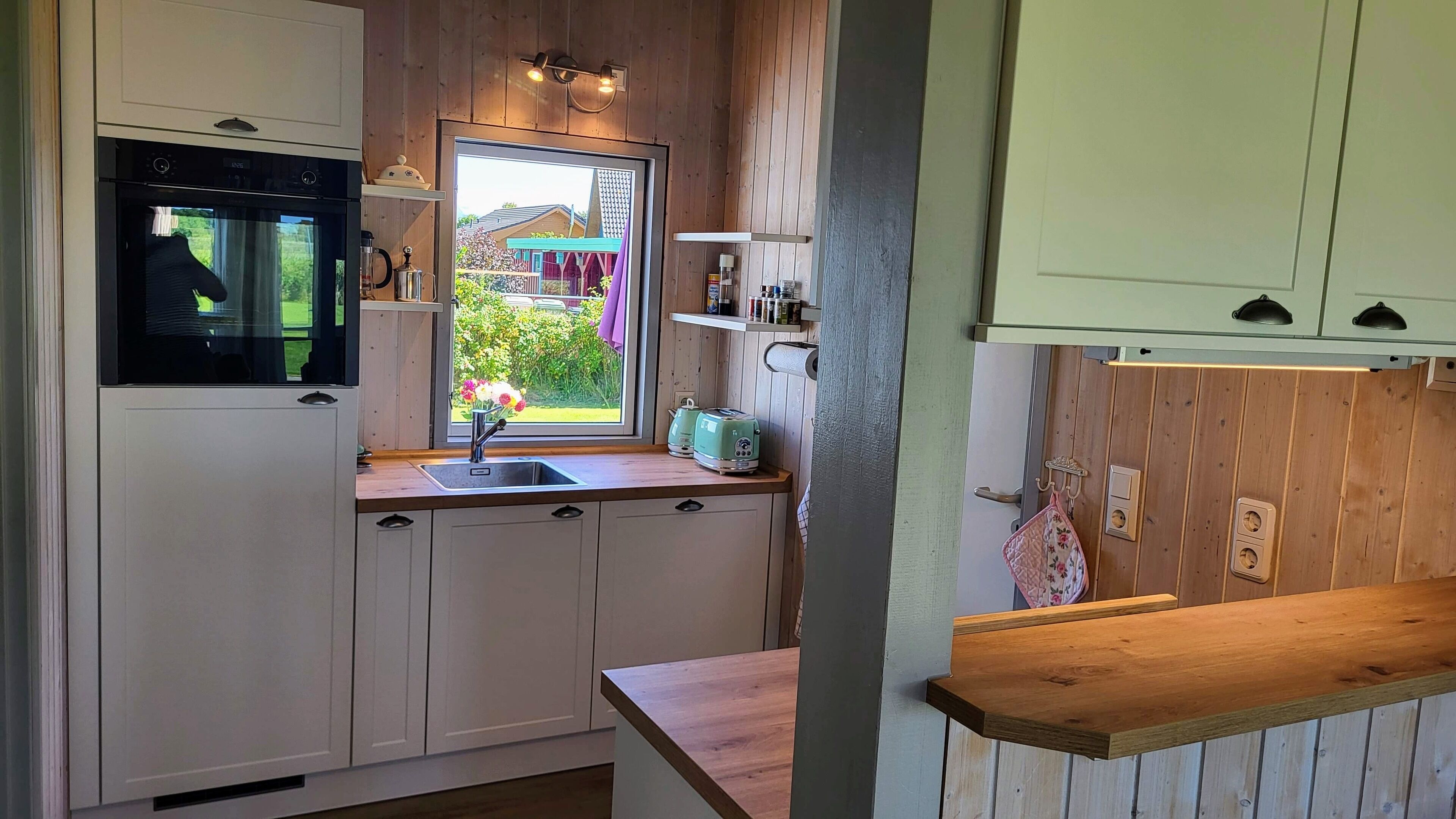 Una cocina con armarios de madera, una ventana con vistas a la vegetación y una encimera con hervidor y tostadora.