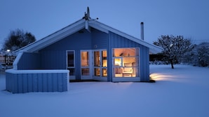 A cozy cabin with a snow-covered exterior, large windows, and a visible interior with a warm light. - Bright Danish wooden house with unobstructed views of the countryside, pets welcome (Kating)