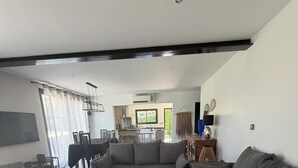 A modern living room with a large sectional sofa, a wooden coffee table with magazines, a dining area with chairs, and a kitchen in the background. - Villa 220m2, land 3000m2, 5 "village on foot, 4km Saint-Rémy-de-Provence (Eyragues)