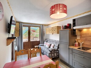 A compact kitchen with a dining area, a sofa, and a TV mounted on the wall.