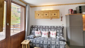 A cozy room with a patterned sofa, wooden cabinets, and a view through a large window. - Ski-in/ski-out: 2 rooms, 5 ppl, terrace, free parking, WiFi (Les Menuires)