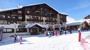 A ski resort with a large building with multiple balconies and a ski lift nearby. - Ski-in/ski-out: 2 rooms, 5 ppl, terrace, free parking, WiFi (Les Menuires)
