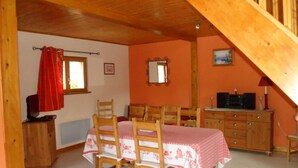 A dining area with a table set for four, wooden chairs, a wooden cabinet, a mirror, and a window with a red curtain.