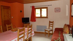 A cozy room with a wooden ceiling, a dining table with chairs, a television, a window with curtains, and a sofa.