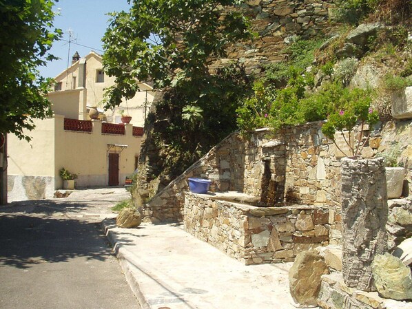 A narrow street with stone buildings, one with a blue basin on its ledge.