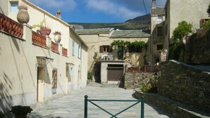 A narrow street with stone walls and buildings, a metal gate in the center, and a mountain in the background.