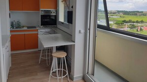 Une cuisine moderne avec des meubles de couleur orange, un four encastré et une grande fenêtre donnant sur un paysage rural.