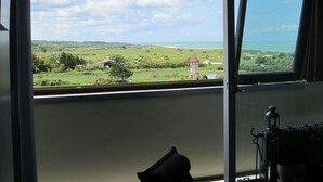 Une pièce dotée d’une grande fenêtre donnant sur un paysage verdoyant, avec une tour et un bâtiment au toit rouge.