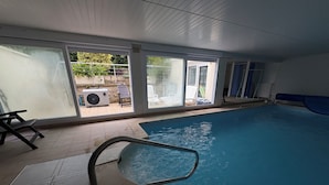An indoor swimming pool with a clear view of the outside, a poolside chair, and a water filtration system. - quiet comfort cottage, sea view, terraces and heated indoor pool (Ver-Sur-Mer)
