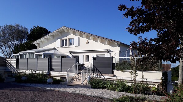 A modern two-story house with a covered patio, a gated entrance, and a stone pathway leading to the door. - quiet comfort cottage, sea view, terraces and heated indoor pool (Ver-Sur-Mer)