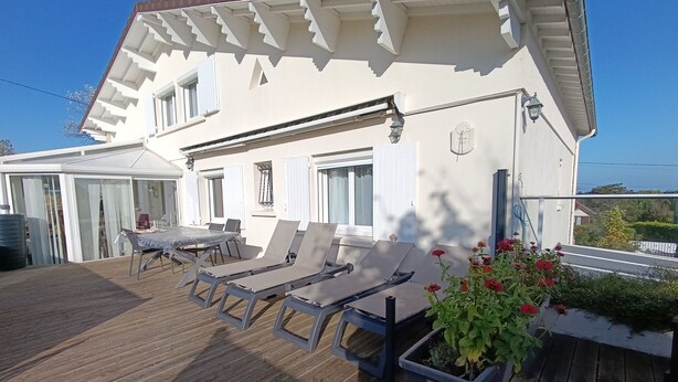 A white building with a wooden deck, outdoor seating, and a potted plant. - quiet comfort cottage, sea view, terraces and heated indoor pool (Ver-Sur-Mer)