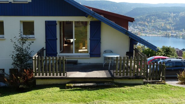Une maison avec un toit bleu, une clôture en bois et une vue sur un lac et des montagnes.