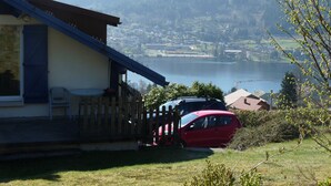 Une propriété située au bord d’un lac, dotée d’une terrasse en bois et d’une voiture rouge garée devant.