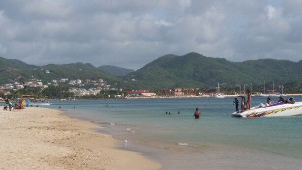 A beach with clear water, people swimming, and boats. There are buildings in the background and mountains. - Beautiful Condo with Fantastic Sea and Sunset Views (Cap Estate)