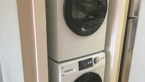 Een wasmachine en droger boven elkaar in een kamer met houten vloeren en witte muren.