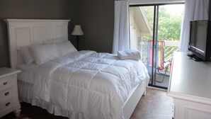 Een slaapkamer met een groot bed, een televisie en een balkon met uitzicht op groen.