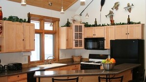 Une cuisine avec des meubles de rangement en bois, un réfrigérateur noir, une cuisinière et un panier de fruits posé sur le plan de travail.
