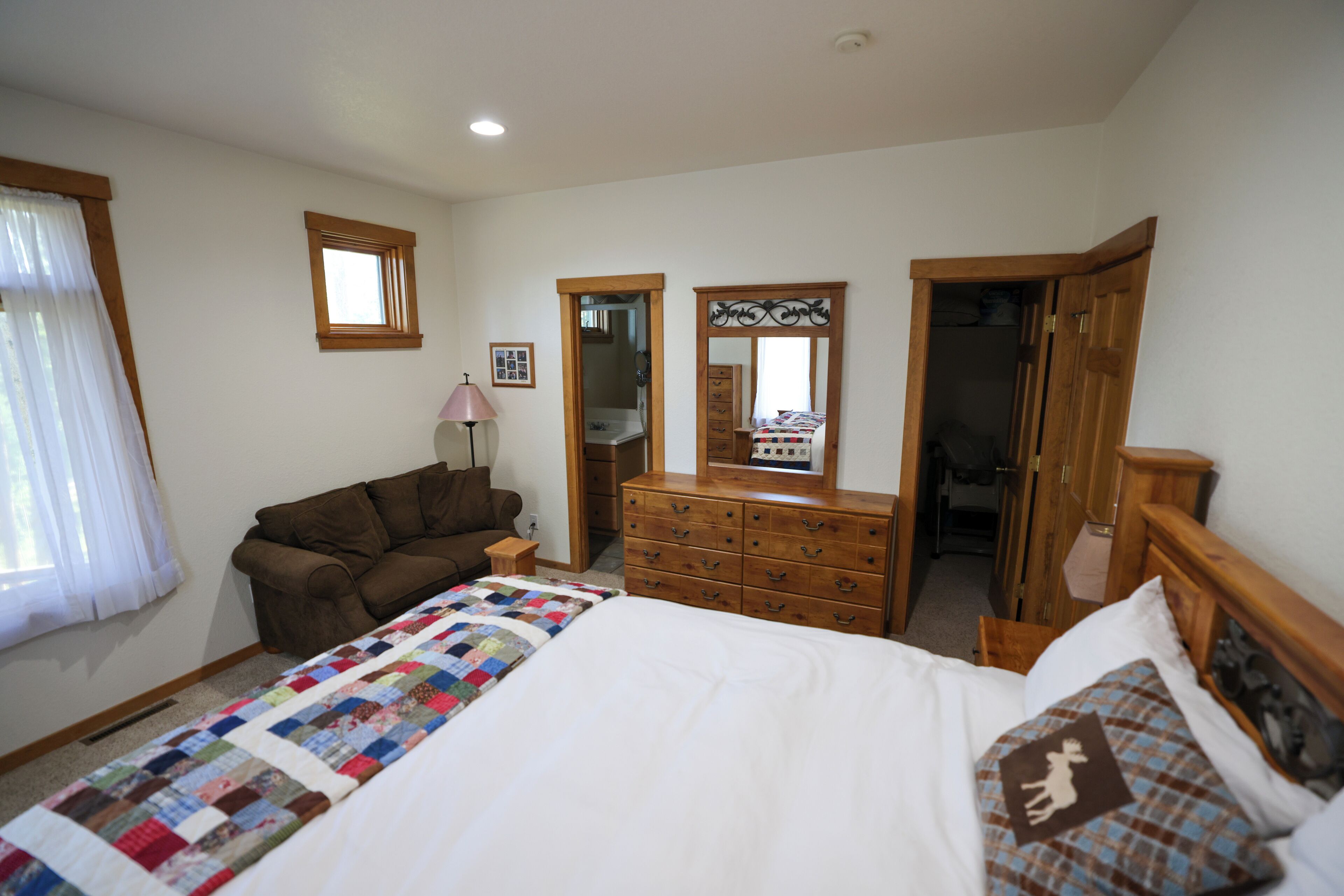 Un dormitorio con una cama, un aparador, un espejo, una ventana con cortinas y una puerta de madera.