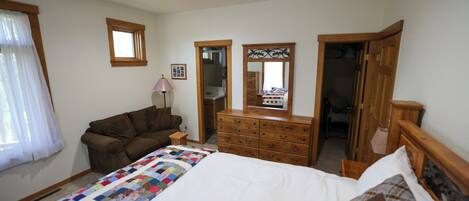 Un dormitorio con una cama, un aparador, un espejo, una ventana con cortinas y una puerta de madera.