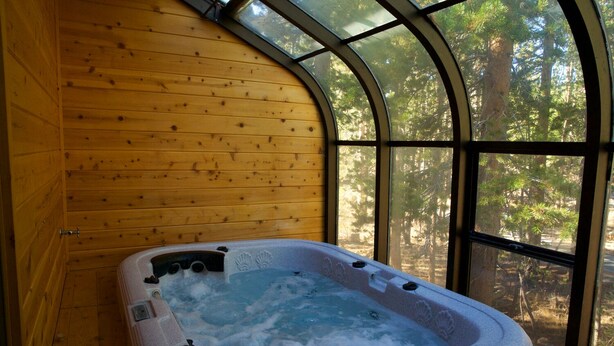 Una vasca idromassaggio in una cabina di legno con una finestra ad arco che si affaccia sulla foresta.