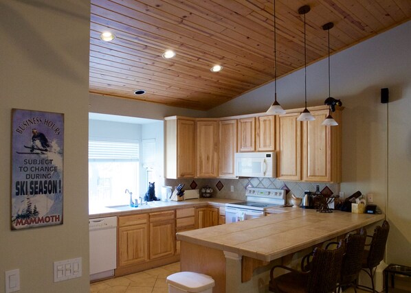 A kitchen with wooden cabinets, a central island, pendant lights, and a poster on the wall.