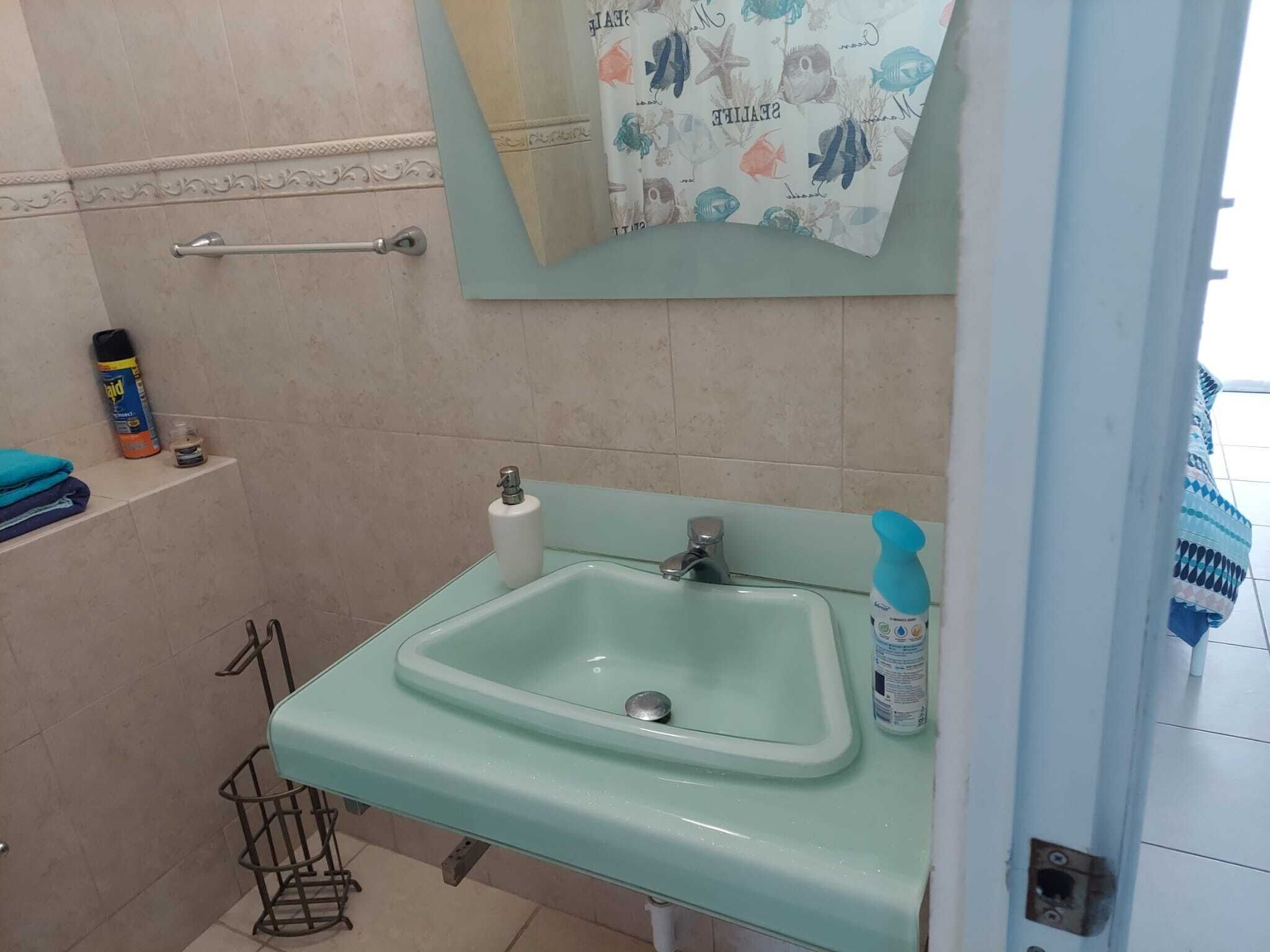 A bathroom with a light blue sink, a towel rack, a shelf with toiletries, and a shower area.