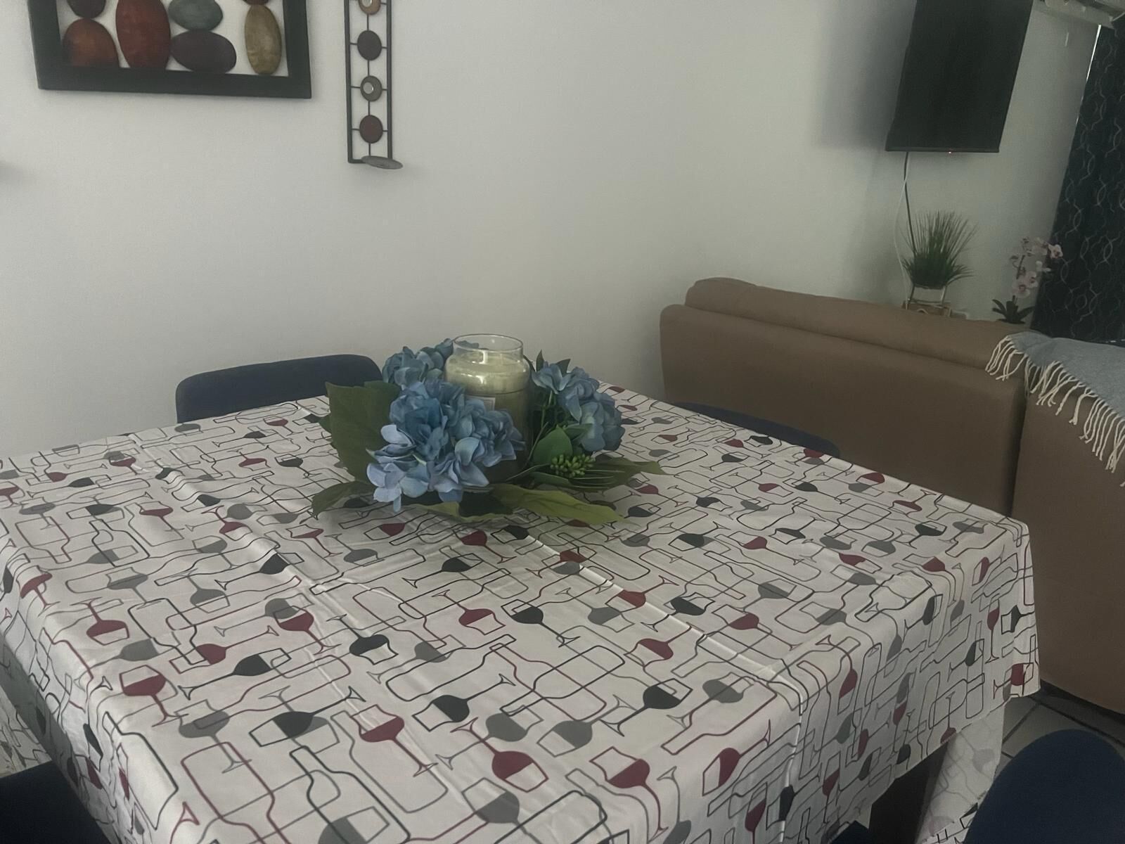 Una mesa de comedor con mantel estampado, un centro de mesa con vela y un sofá al fondo.
