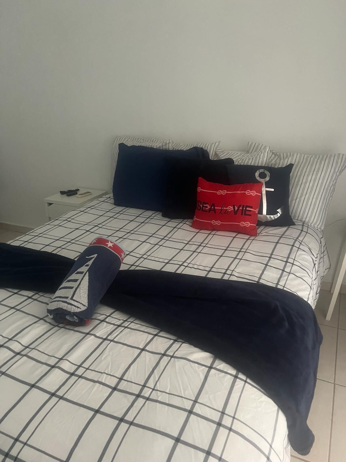A bed with a checkered bedspread, a navy blue blanket, and a red pillow with the text "SEA LOVE".