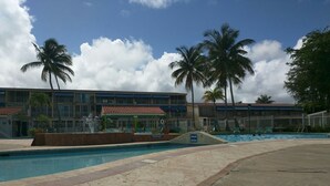A hotel with a swimming pool, palm trees, and a building with a red-tiled roof.