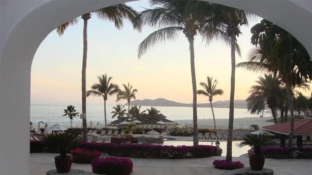 Vista di un resort con piscina, palme e una spiaggia sullo sfondo.