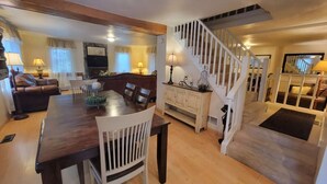 Un vaste espace de vie comprenant une table à manger en bois, des chaises blanches, un canapé et un escalier menant à un autre niveau.