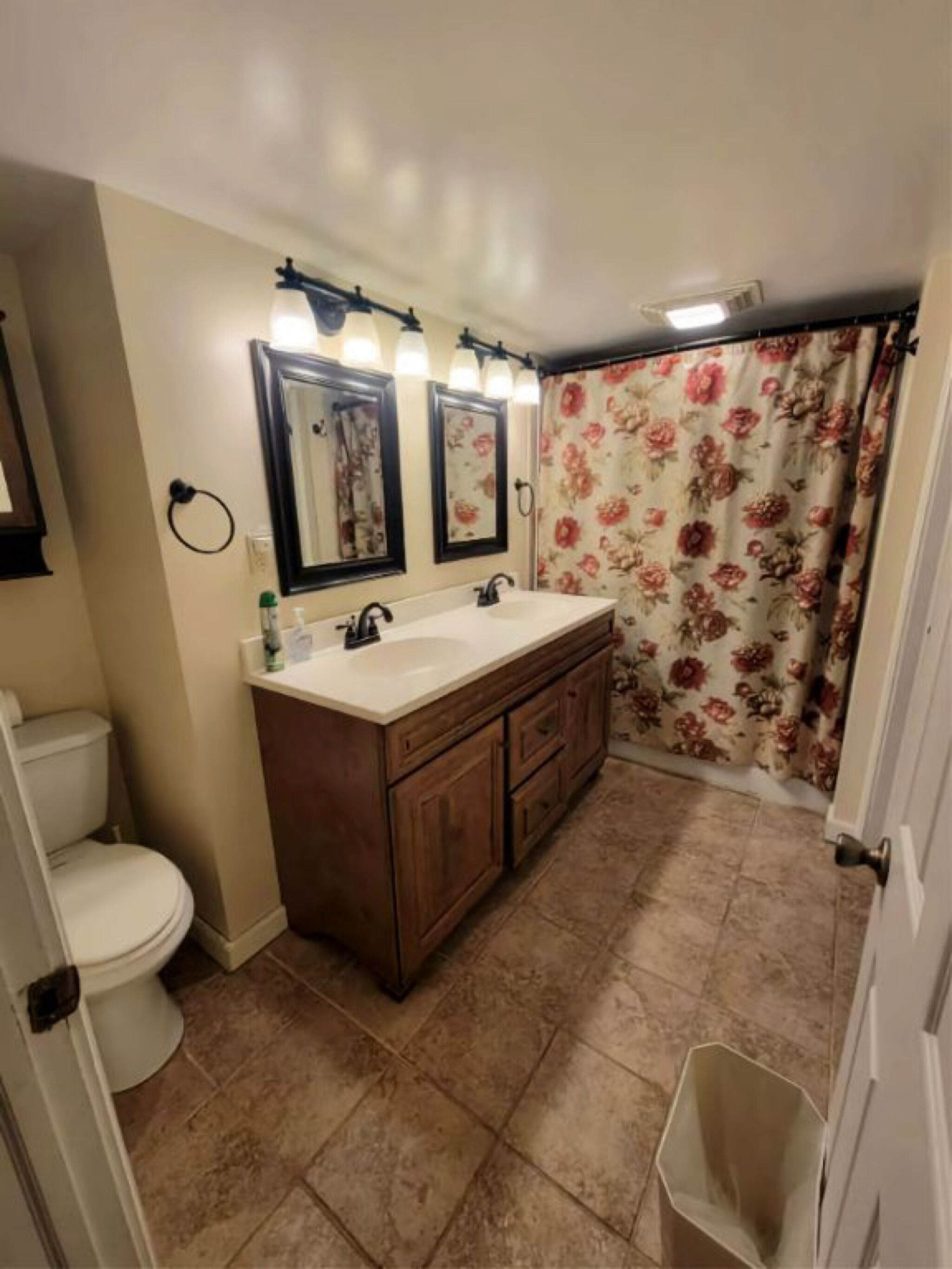 Un bagno con doppio lavabo, un water e una tenda da doccia con motivo floreale.