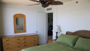 A bedroom with a bed, dresser, mirror, door, and ceiling fan.